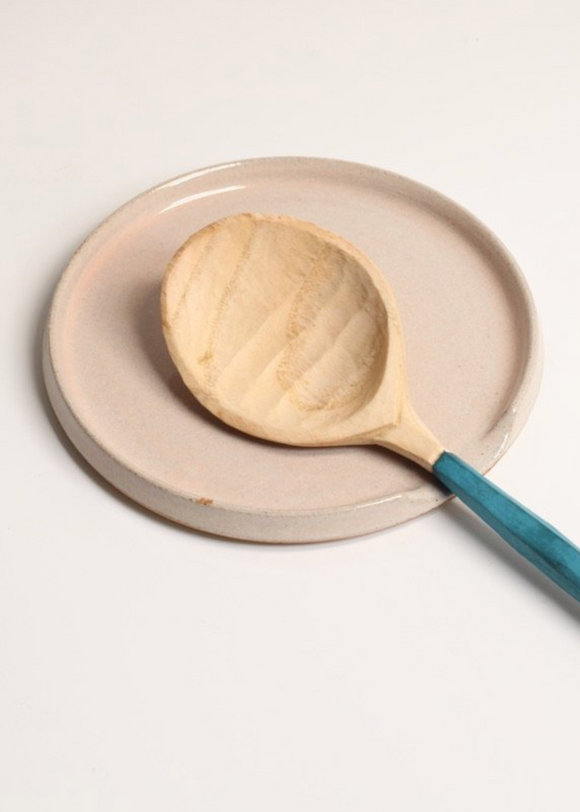 A beige stoneware spoon rest with a satin sea kelp and gloss overlay glaze on a white background, accompanied by a wooden spoon with a blue handle.