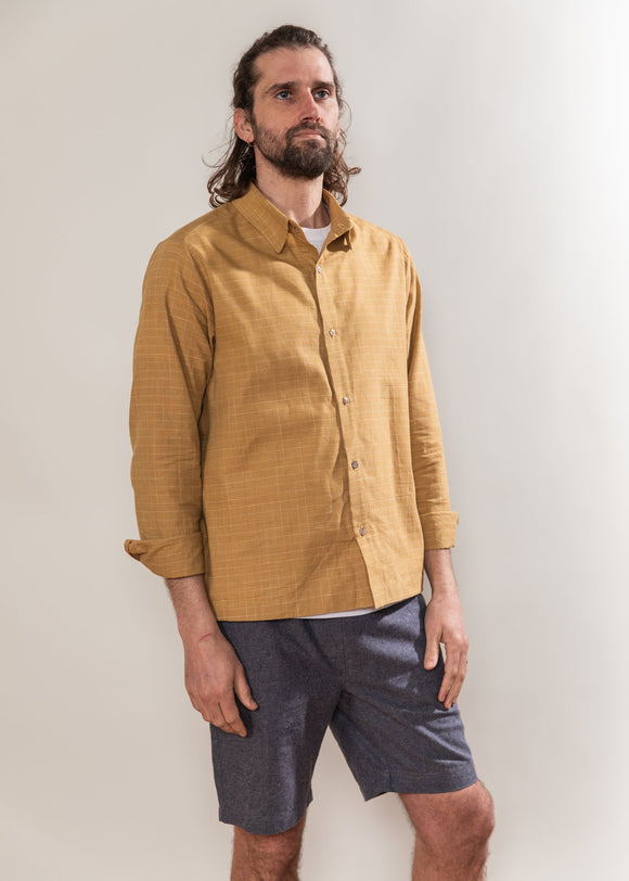 Man wearing a mustard yellow shirt and dark shorts against a plain background