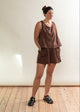 Woman wearing a brown outfit standing against a white wall.