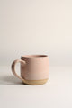 A beige ceramic mug with a handle, placed against a plain background.