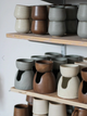 Collection of ceramic pots on wooden shelves with a neutral background