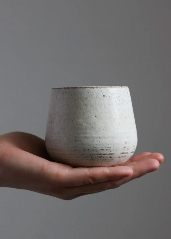Hand holding a ceramic cup against a gray background
