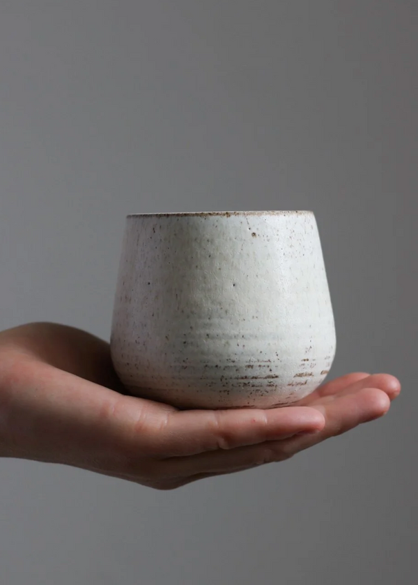 Hand holding a ceramic cup against a gray background