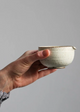 Hand holding a ceramic cup against a plain background