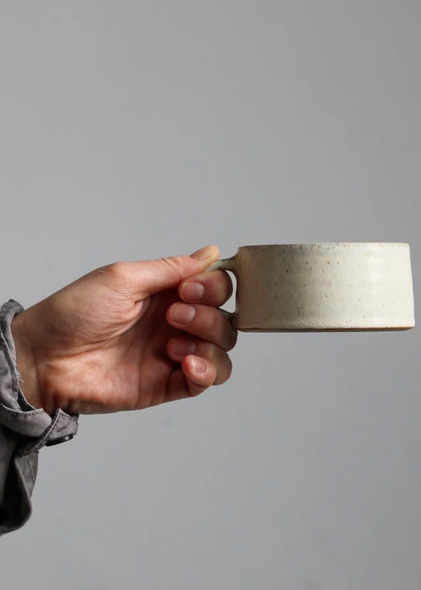 Hand holding a metallic square object against a gray background