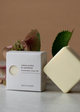 Handmade soap bar and packaging on a neutral background with greenery