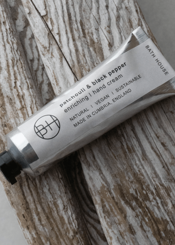 Tube of Bath House Patchouli & Black Pepper hand cream on a wooden surface