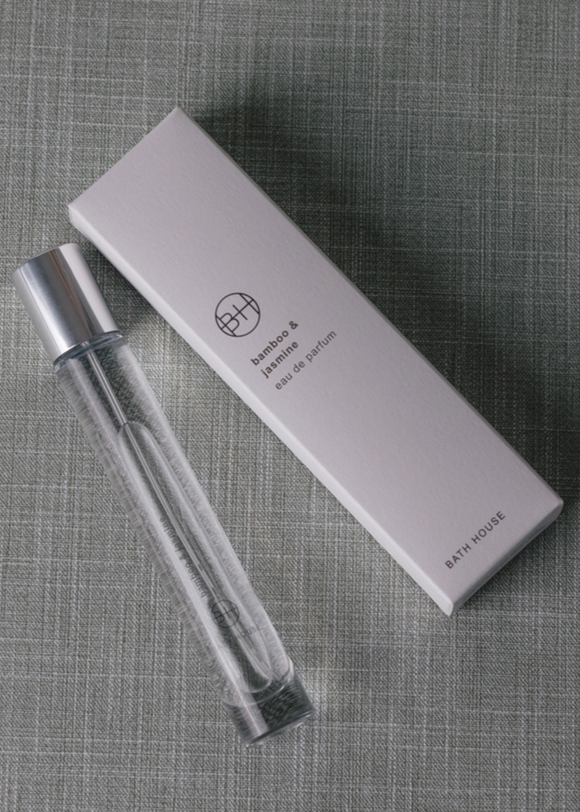 Clear spray perfume bottle with silver top and white box on a textured gray surface