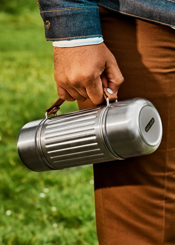 Person holding a silver thermos outdoors on grass
