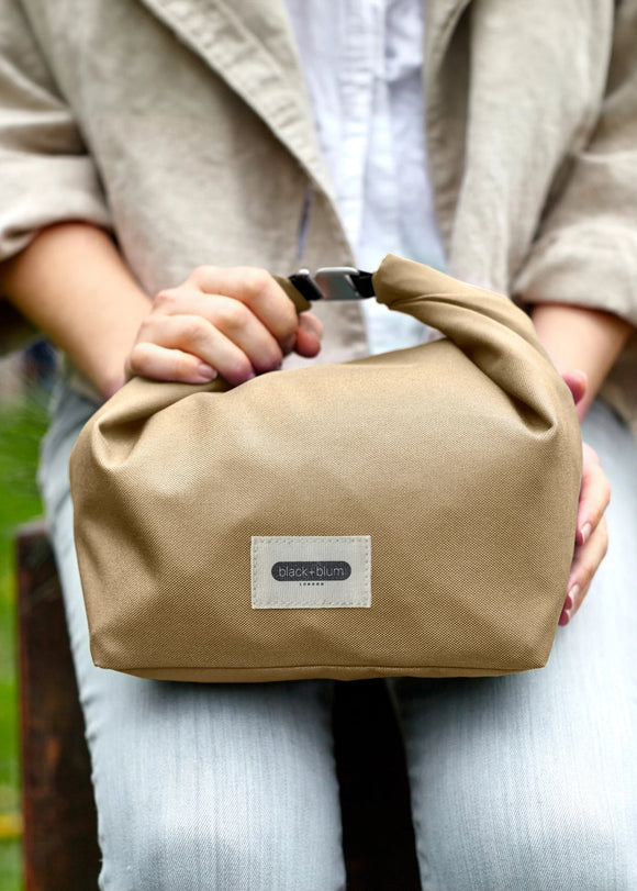 Person holding a beige bag with a visible brand label outdoors.