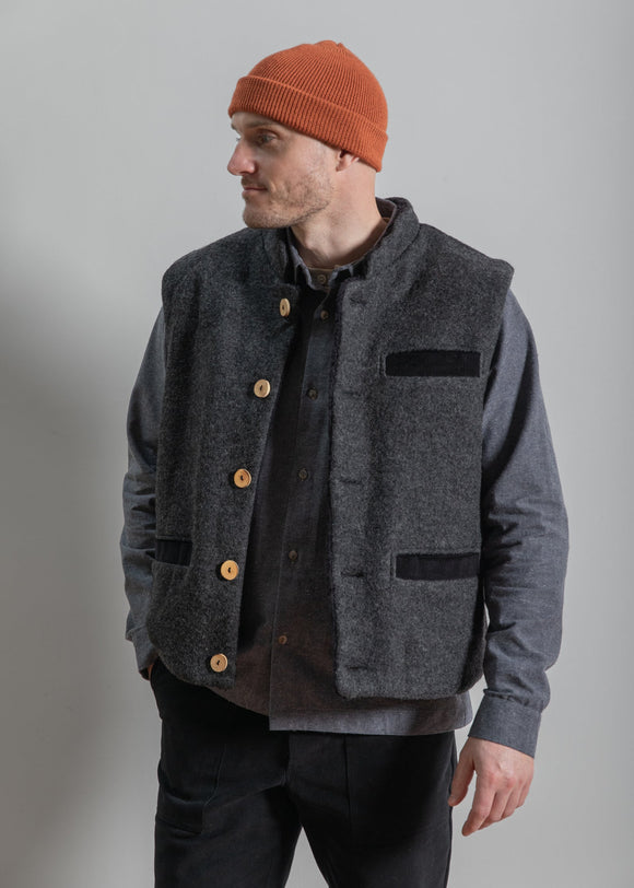 Man wearing a gray vest with black accents and a red beanie against a plain background