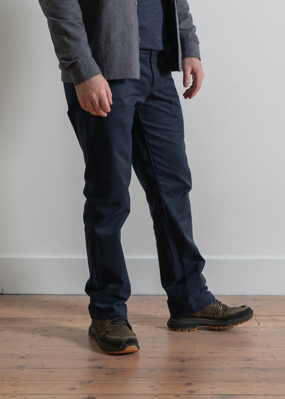 Person wearing dark pants and a gray jacket on a wooden floor with a white wall background