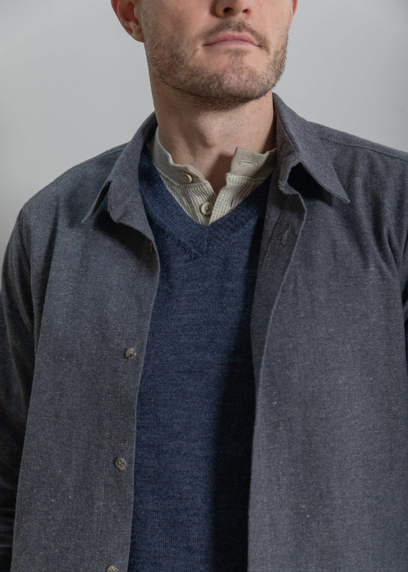 Man wearing a gray jacket over a blue sweater with a plain background