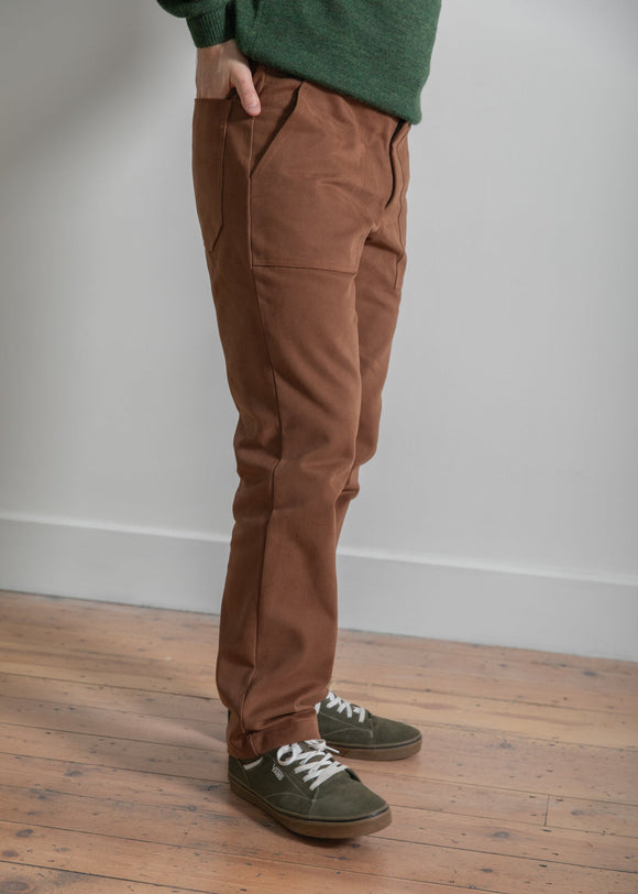 Person wearing brown pants and green shoes on a wooden floor with a white wall background