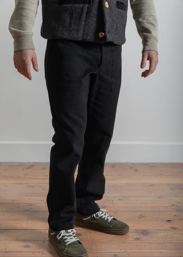 Person wearing a dark vest, black pants, and green shoes on a wooden floor.
