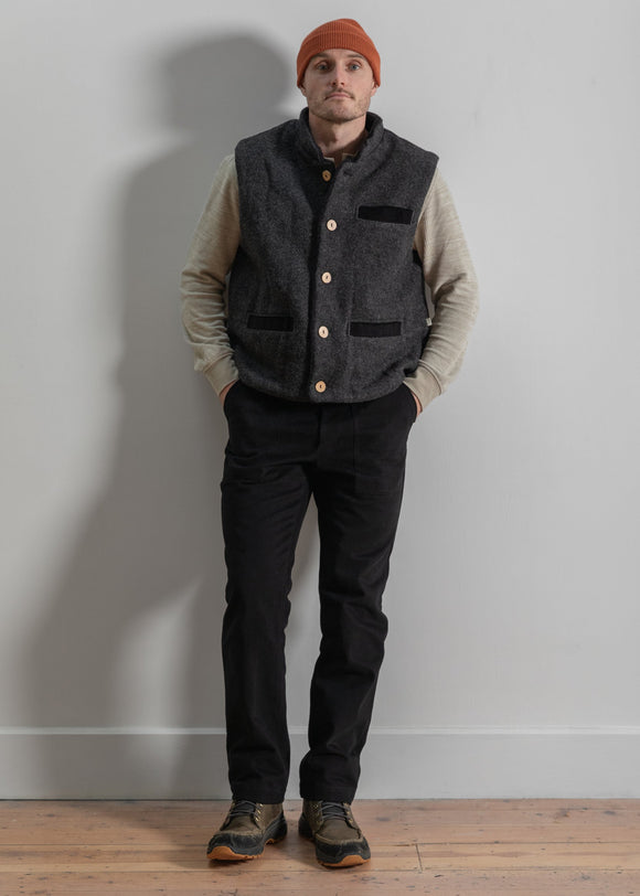 Man wearing a gray vest, black pants, and a red beanie against a plain wall.