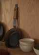 Stack of ceramic bowls on a wooden shelf with pans in the background