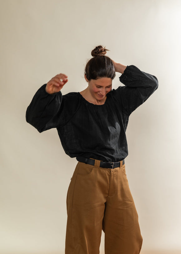 Person wearing a black sweatshirt and brown pants against a plain background