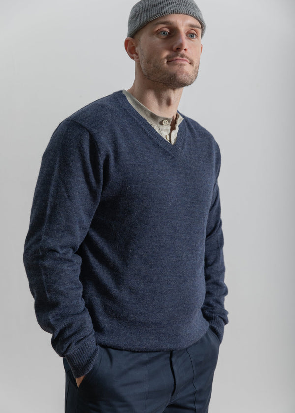 Man wearing a blue sweater and gray beanie against a plain background