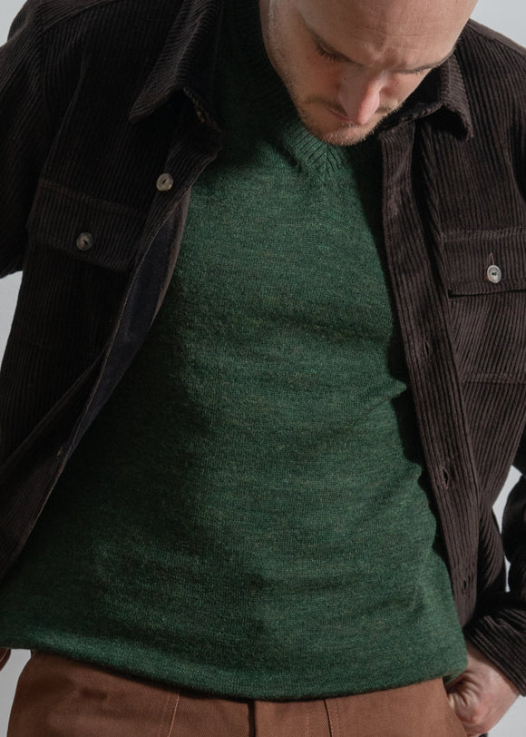 Man wearing a green sweater and brown jacket against a white background