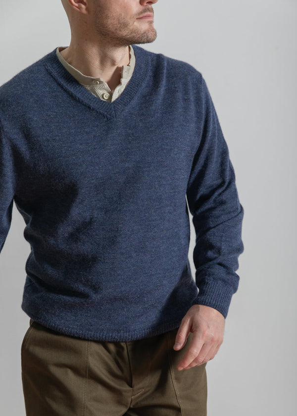 Man wearing a blue sweater and brown pants against a plain background