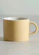 pale yellow mug on a light gray surface with a neutral background
