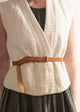 Person wearing a beige sleeveless top with a brown belt and dark skirt.