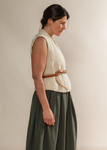 Woman wearing a cream sleeveless top and green skirt against a plain background
