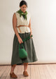 Woman in a white sleeveless top and green skirt holding a green bag against a plain background