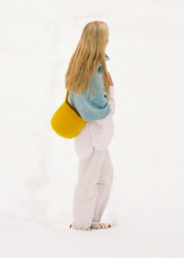 Person wearing a blue knitted shawl and yellow bag on a white background