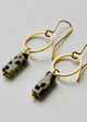 Gold hoop earrings with black and white bead drops on a light gray background