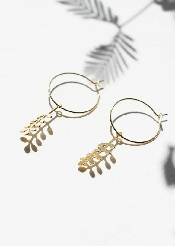Gold hoop earrings with leaf-like designs on a light background