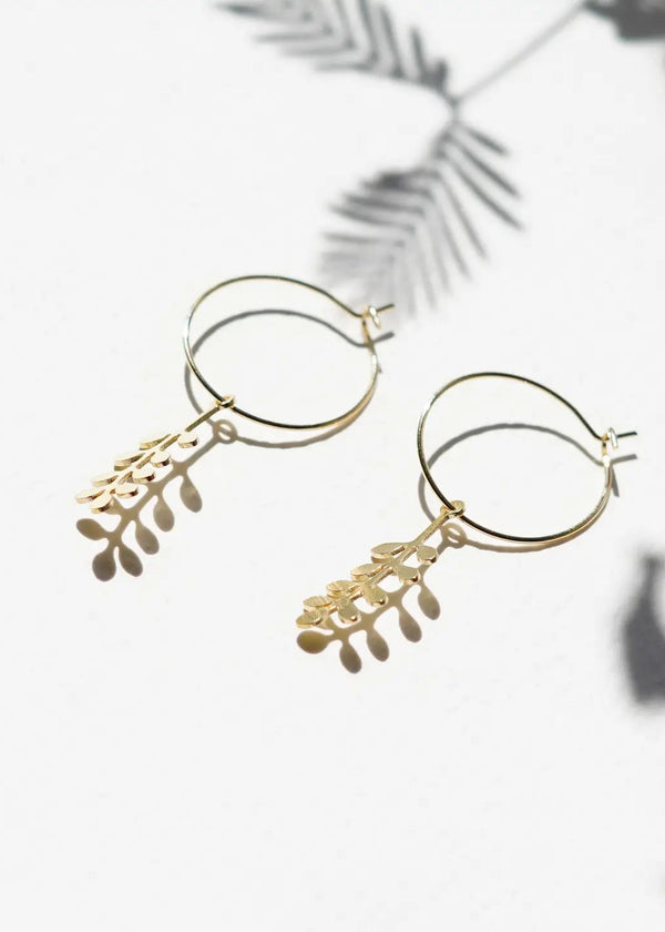 Gold hoop earrings with leaf-like designs on a light background