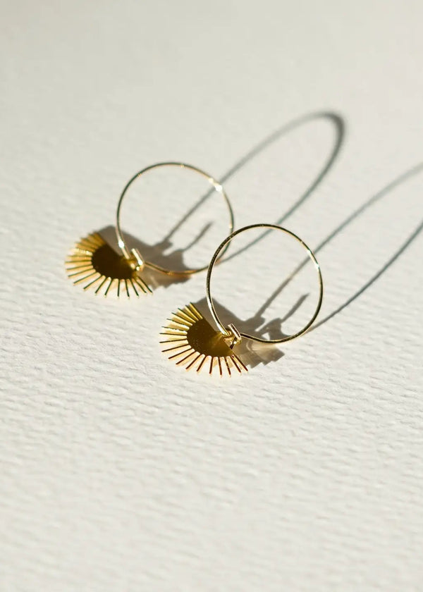 Gold hoop earrings with sunburst designs on a light background