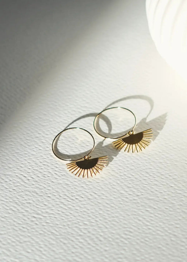 Gold hoop earrings with sunburst designs on a textured white surface