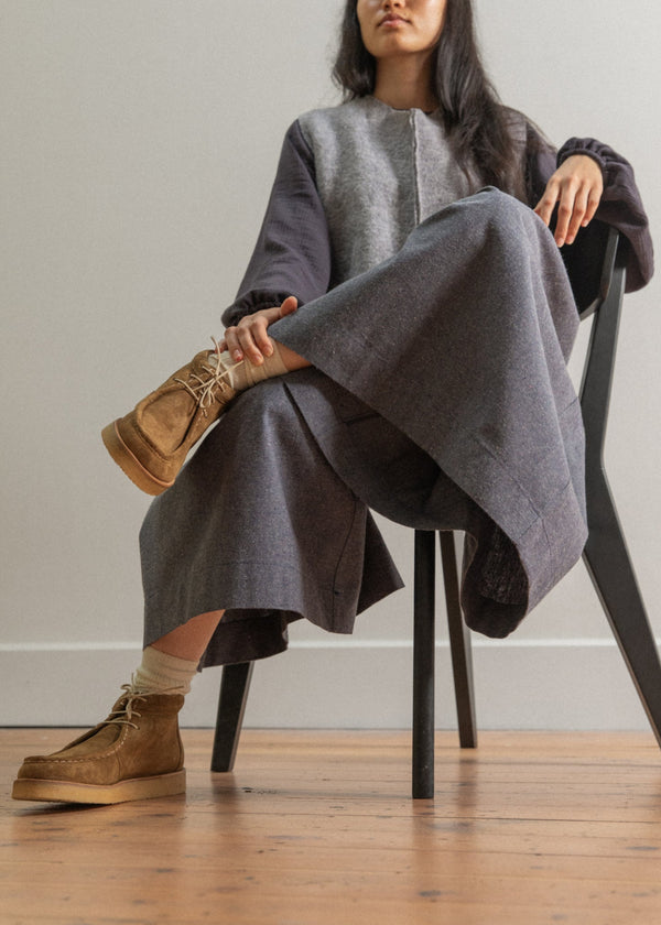 Woman sitting on a chair wearing a long gray coat and brown boots.