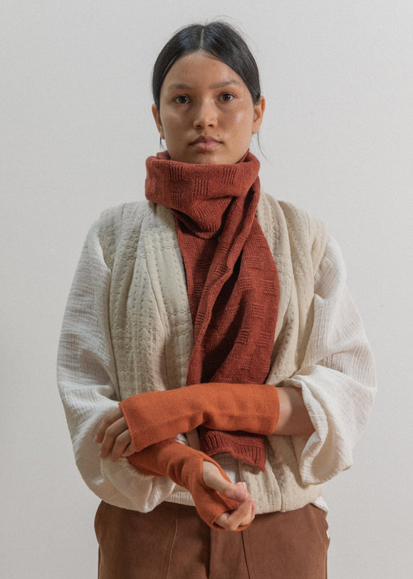 Person wearing a beige sweater and rust-colored scarf against a plain background