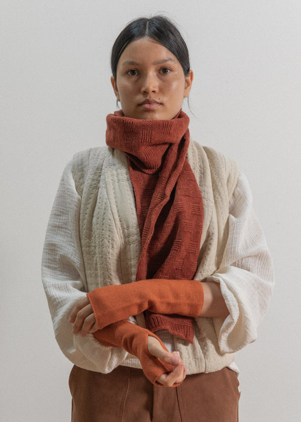 Person wearing a beige sweater and rust-colored scarf against a plain background