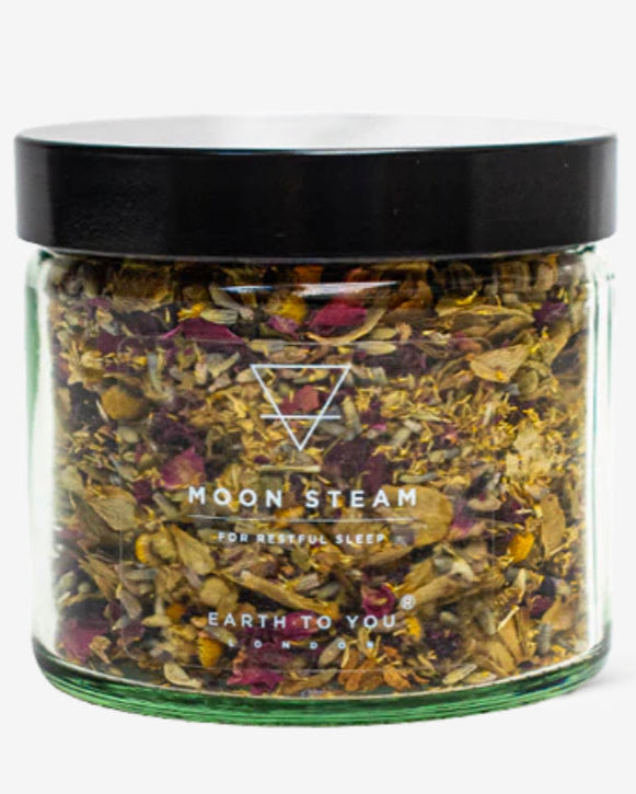A clear glass jar containing a blend of dried herbs and flowers labeled as 'Moon Steam' for skincare purposes.