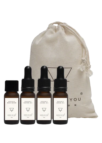 A set of four small dropper bottles containing organic skincare oils, positioned in front of a beige drawstring bag with a leaf logo.