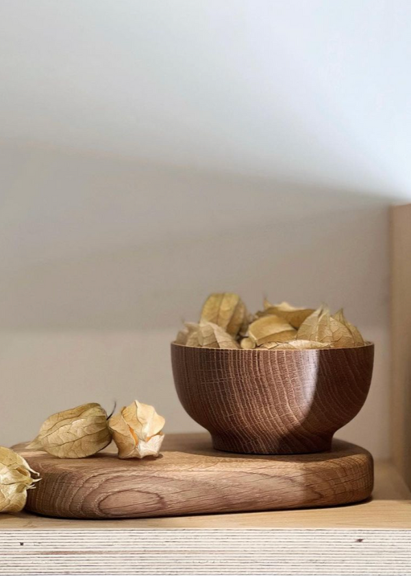 A hand-turned oak bowl filled with small small fruit, placed on a wooden table with a larger piece of wood in the background.