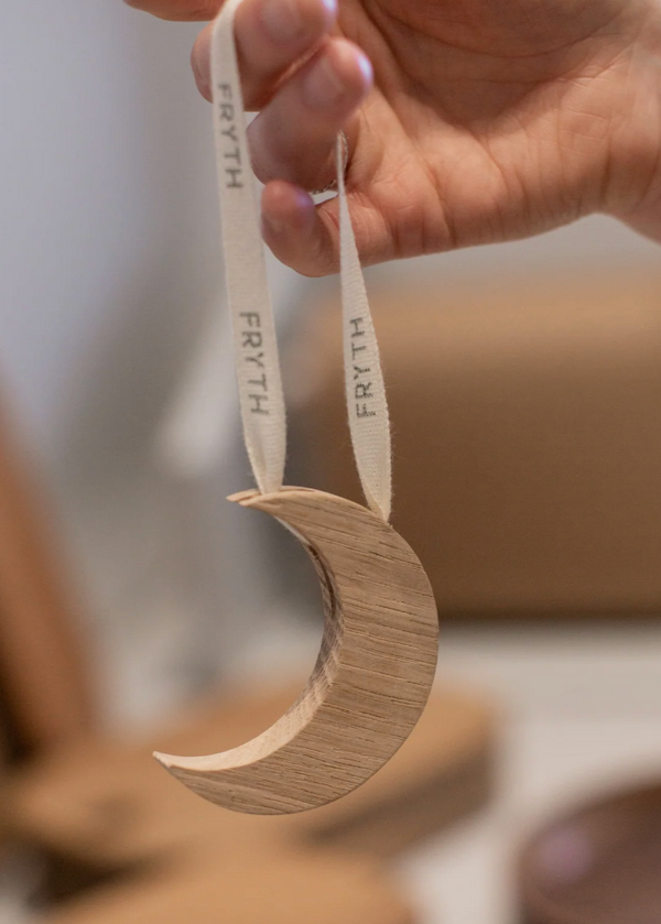 Wooden crescent moon ornament with 'Fryth' branding held by a hand.