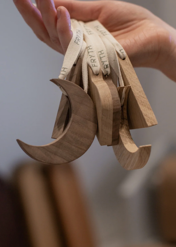 A hand holding a set of wooden crescent-shaped Christmas decorations with visible grain patterns, indicating they are made from wood.