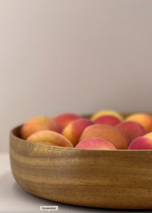Wooden bowl filled with peaches on a light background