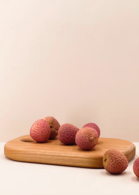 A wooden chopping board with several Exotic fruits on it, placed against a neutral background.