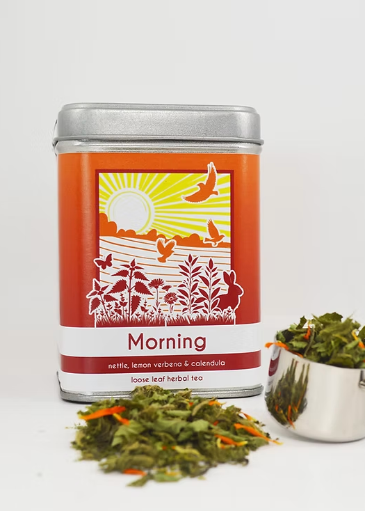 Tea canister labeled 'Morning' with dried tea leaves and a measuring spoon on a white background