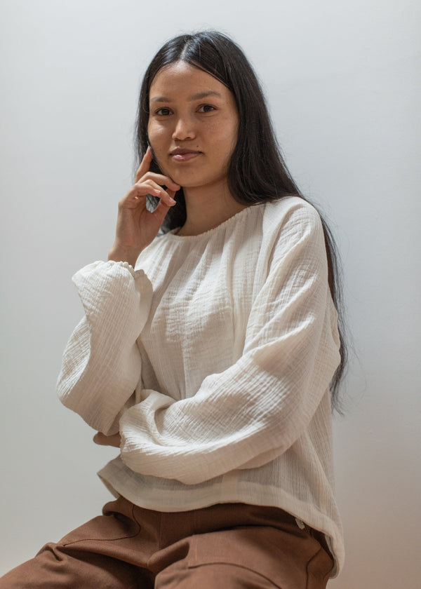 Woman wearing a white top and brown pants against a plain background