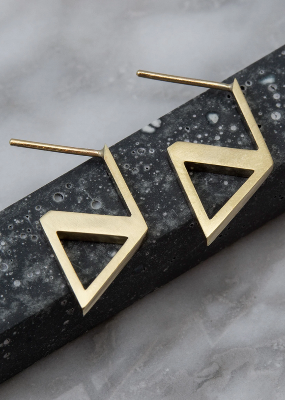 Gold triangle-shaped earrings on a textured black and gray surface