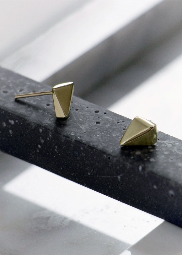 Gold pyramid-shaped earrings on a textured black surface with a light background