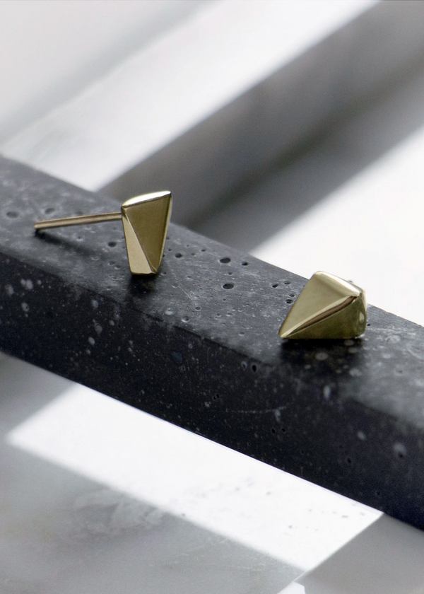 Gold pyramid-shaped earrings on a textured black surface with a light background